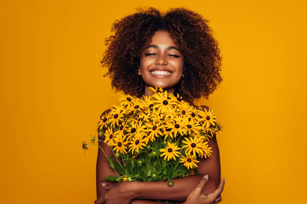 Femme souriante tenant un bouquet de fleurs jaunes, image illustrant la joie et la confiance en soi

